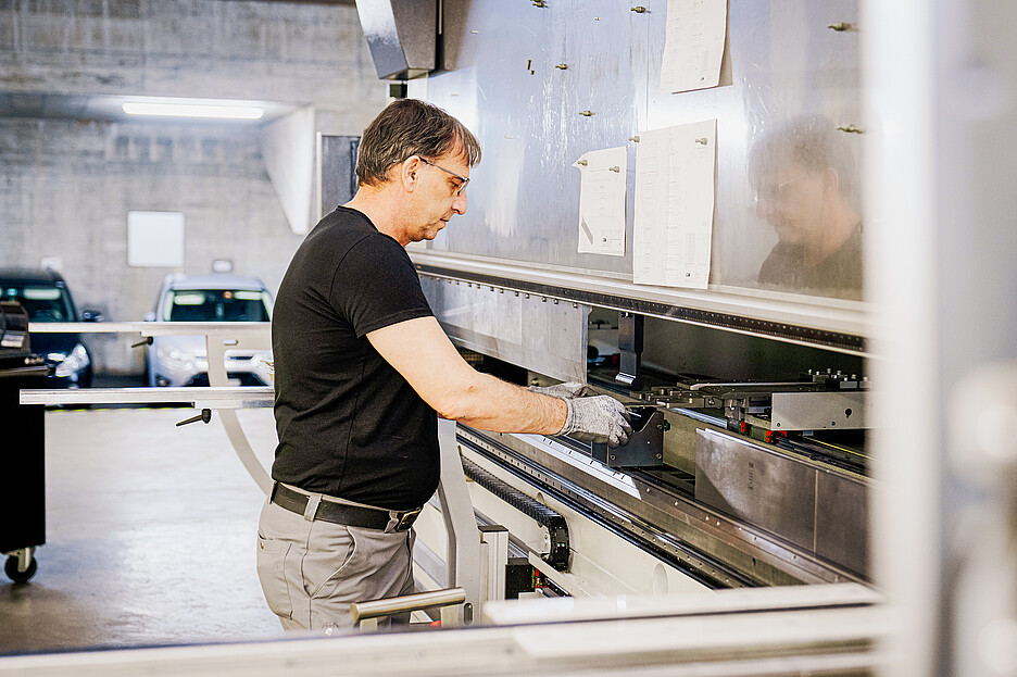 Sadat Ljazami devant une presse plieuse sur laquelle les panneaux découpés sont pliés à la forme souhaitée.