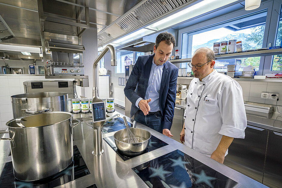 Adrian Seeholzer, responsable régional des ventes chez Menu System (à gauche) avec la cuisinière dernier cri avec laquelle le chef de cuisine Patrick Weber (à droite) et son équipe cuisinent depuis un an pour les hôtes de la «Residenz Am Schärme».